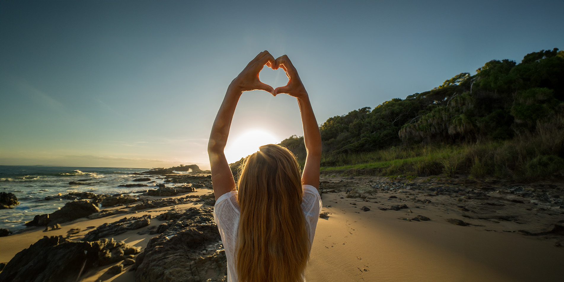 person-with-hand-heart-shape-with-sun-on-beach